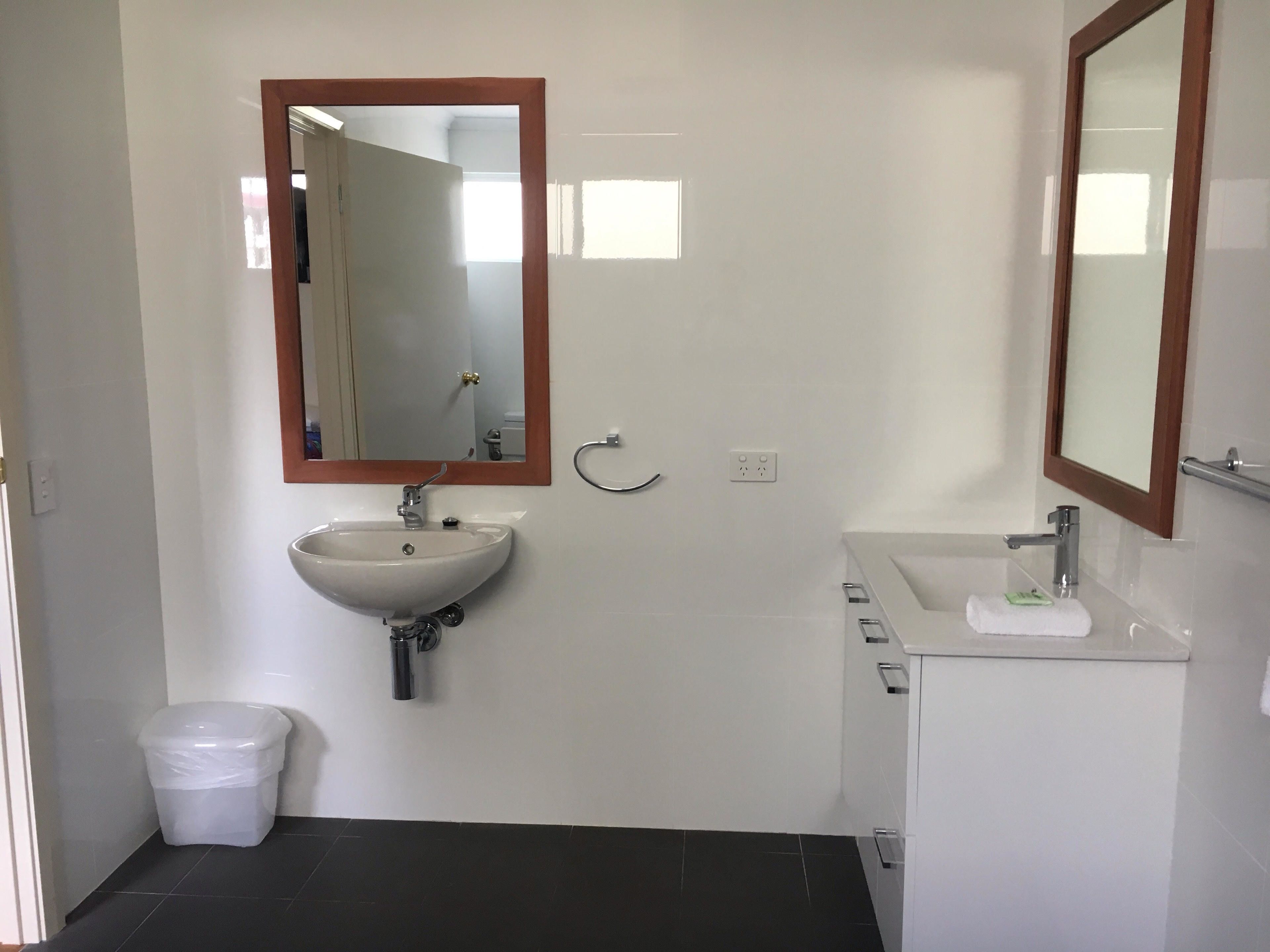 Et badeværelse med hvid vask, spejl, toilet og bruseniche.