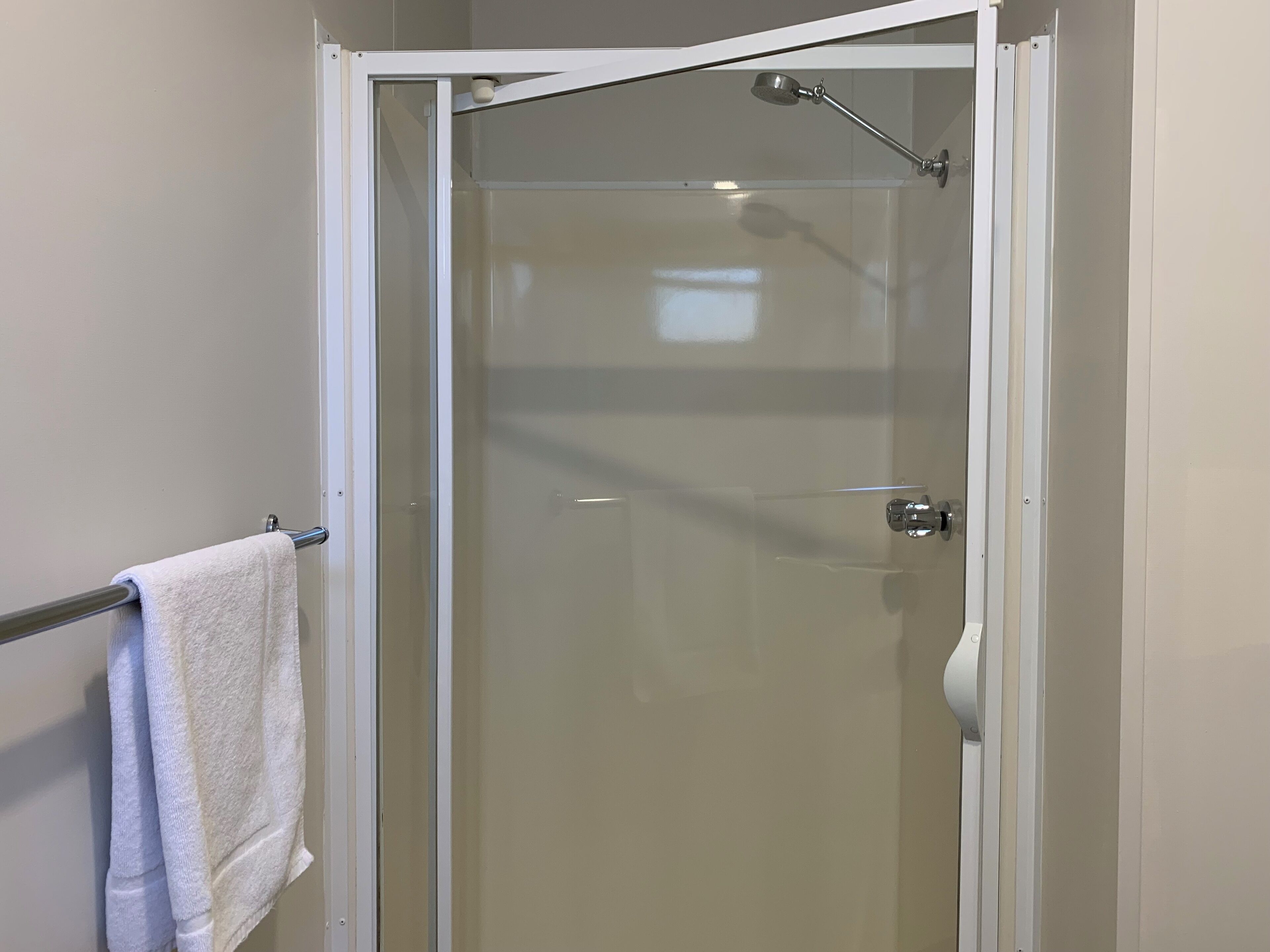 Cabina doccia in vetro con cornice bianca, portasciugamani con asciugamano e soffione visibile.