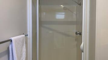 A glass-enclosed shower with a white frame, a towel rack with a towel, and a visible showerhead.