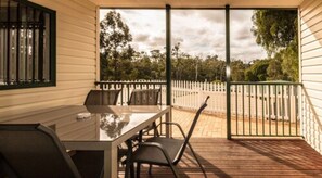 Un patio techado con mesa y sillas, vistas a árboles y una valla.
