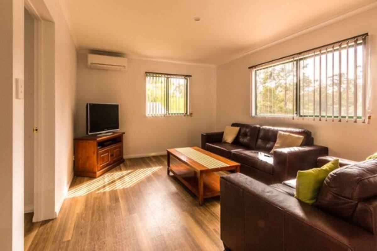Ein Wohnzimmer mit einer braunen Ledersofa, einem Holztisch, einem Fernseher auf einem Holzschrank und einem Fenster mit Jalousien.