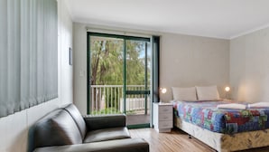 A bedroom with a bed, a nightstand, a dresser, a sofa, and a balcony with a view of trees. - Riverview Tourist Park (Margaret River)