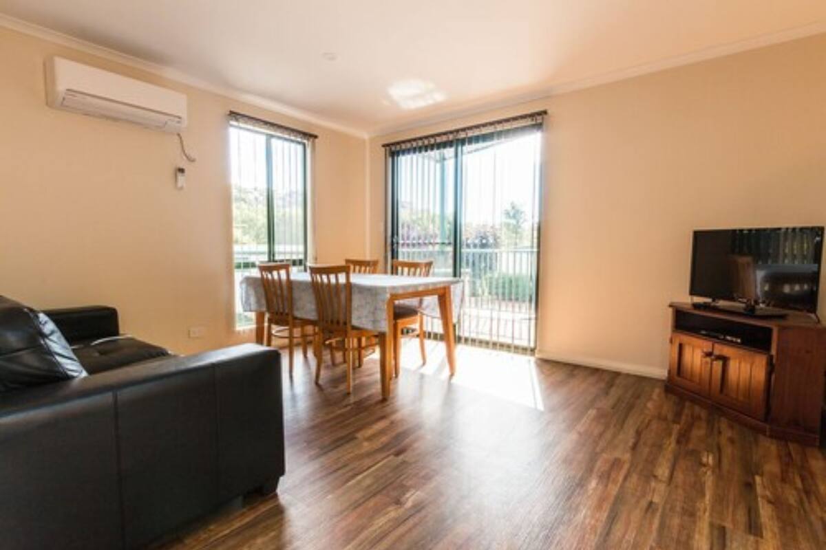 Ein Wohnzimmer mit einer schwarzen Couch, einem Holzespeisetisch mit Stühlen, einer TV-Konsole und einem Balkon mit Blick.