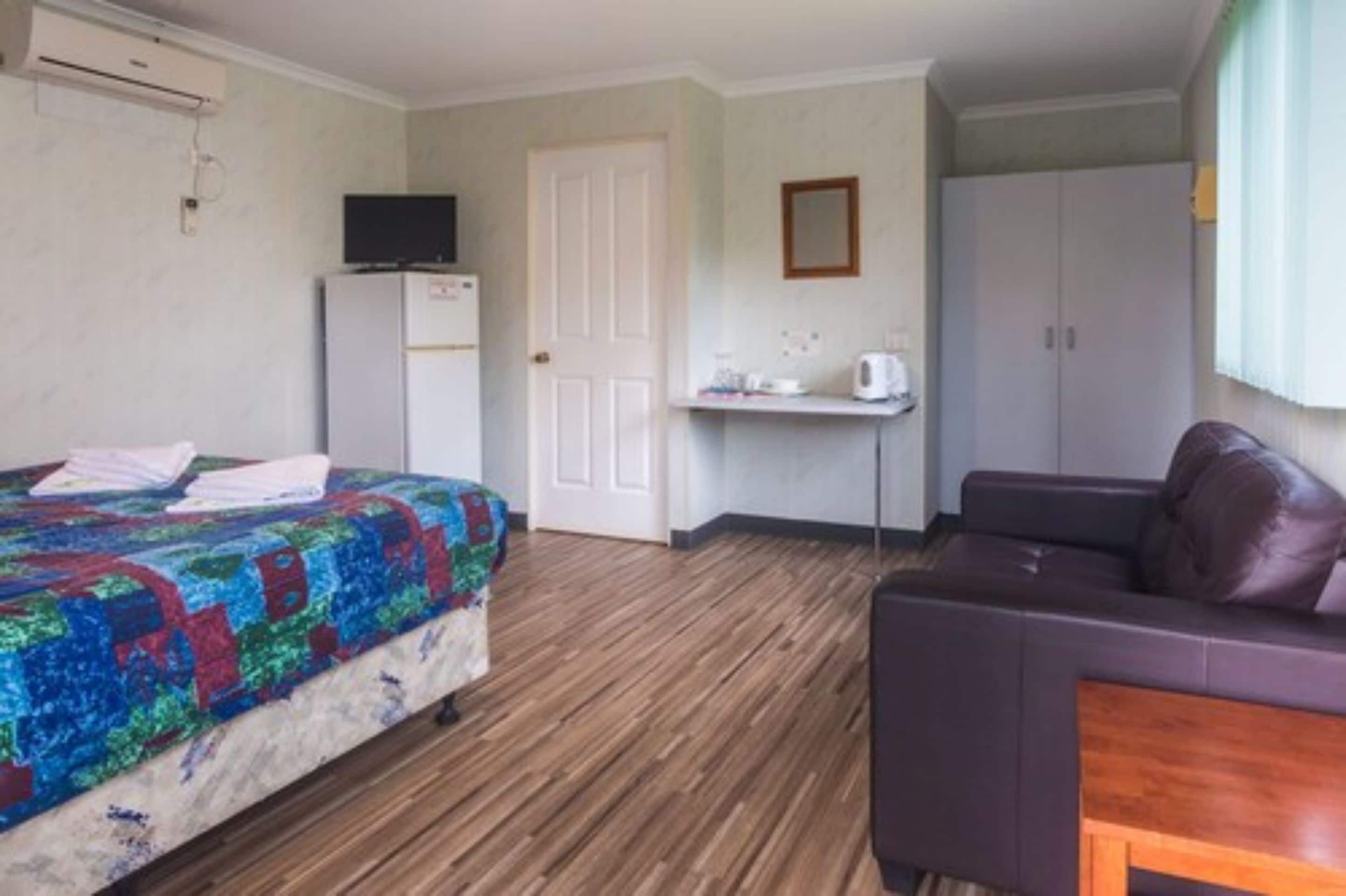 Una habitación con cama, escritorio, silla, armario y televisor.