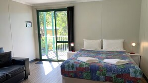 A hotel room with a bed, a desk, a chair, and a sliding glass door leading to an outdoor area. - Riverview Tourist Park (Margaret River)