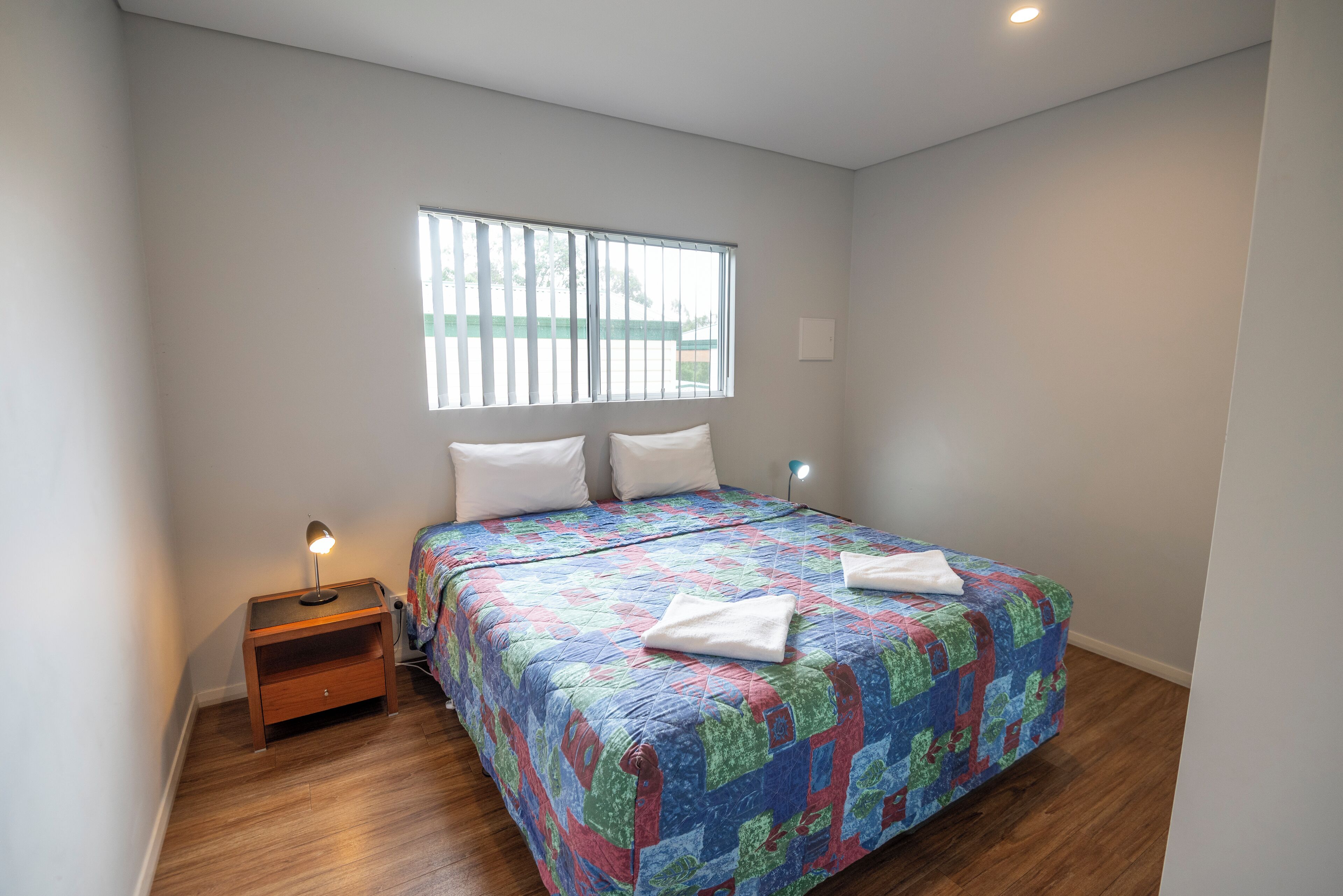 Quarto com uma cama, mesa de cabeceira, janela e luminária na parede.