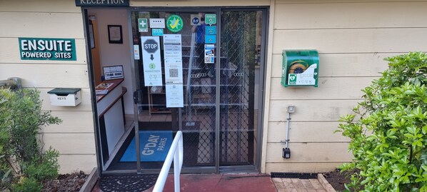 A reception area with a sign for 'ENSUITE POWERED SITES', a 'STOP' sign, and a 'G'DAY PARKS' mat.
