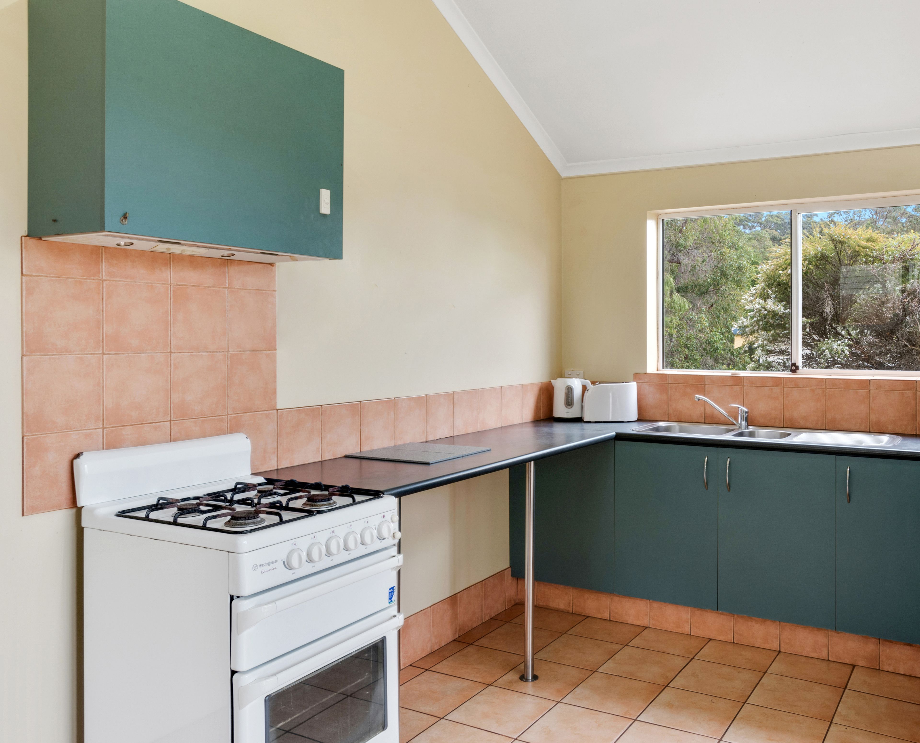 Een keuken met een gasfornuis, oven en een raam met uitzicht op bomen.