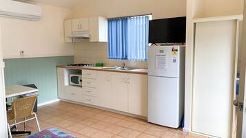 A compact kitchen with a microwave, stove, and refrigerator. There is a small dining area with a chair and a table.