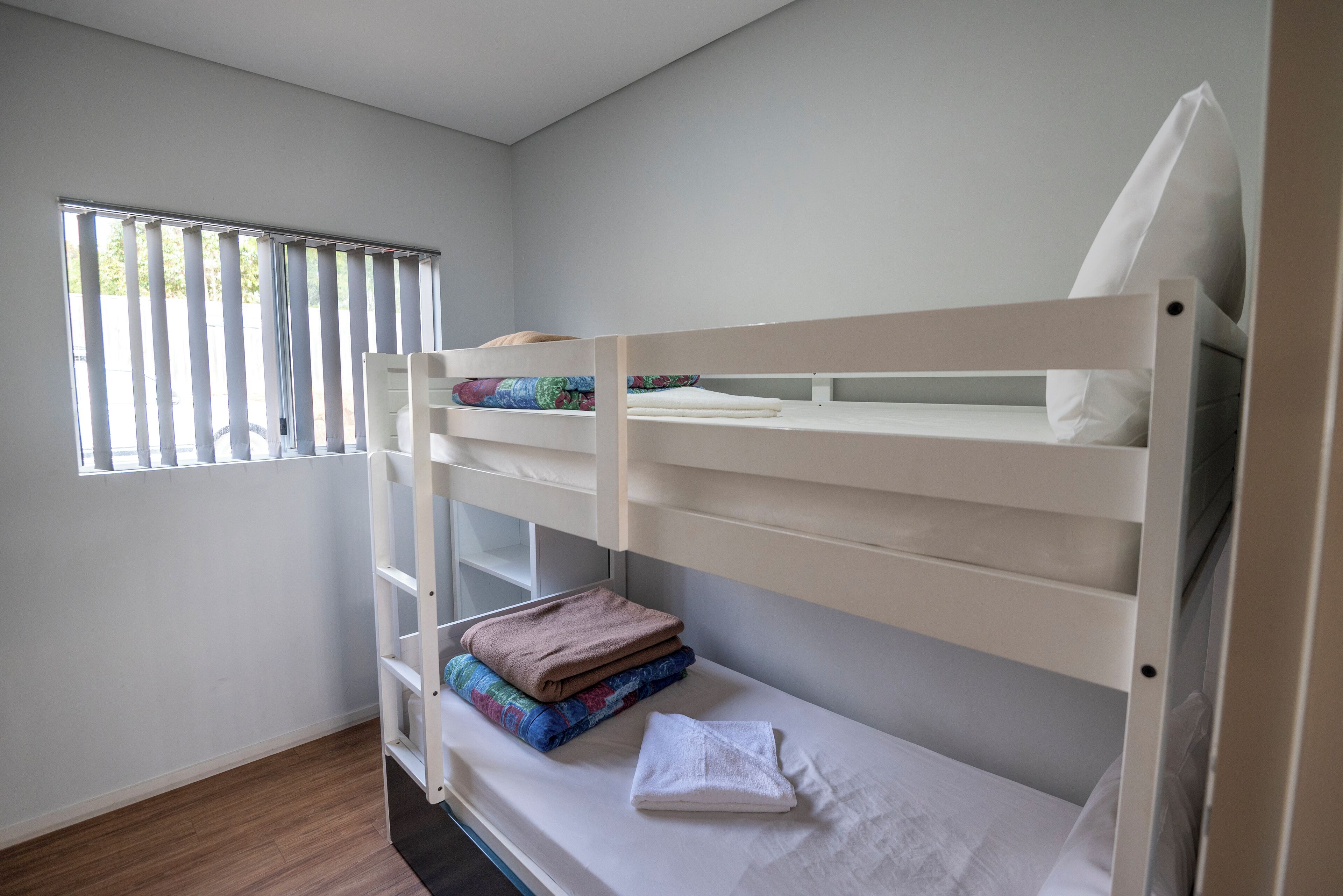 A bunk bed room with a window, a wooden floor, and a white wall.
