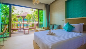 A hotel room with a large bed, a balcony with a view of a building and trees, and a seating area with a chair and table. - Crystal Wild Resort Panwa Phuket (Wichit)