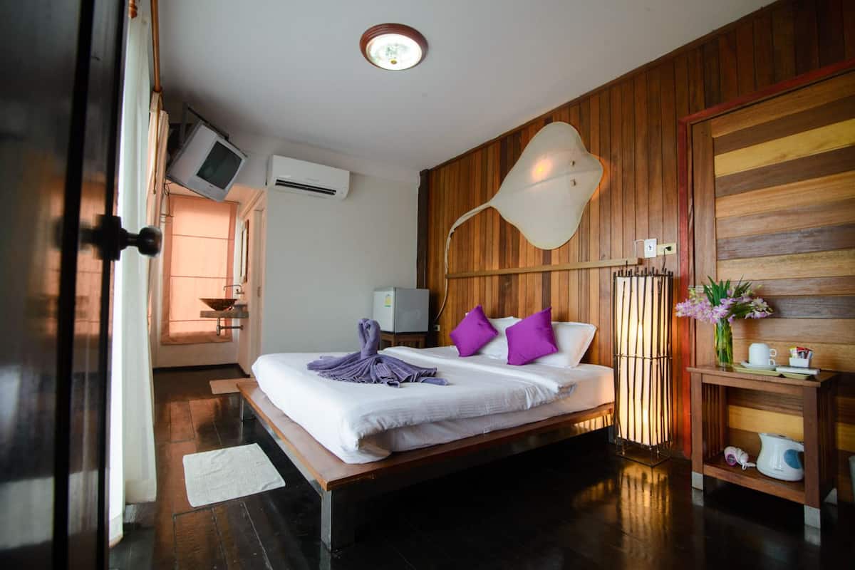 A hotel room with a large bed, a bedside table with a lamp, a wall-mounted TV, and an air conditioning unit.