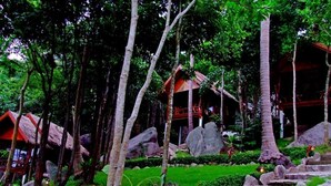 A tropical garden with a stone pathway, palm trees, and a thatched-roof structure.
