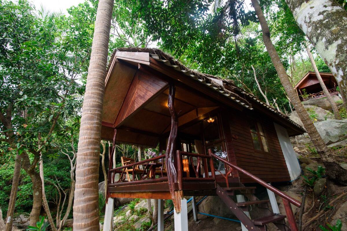 A wooden cabin with a balcony, surrounded by lush greenery and trees.