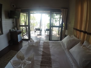 A hotel room with a large bed, a television, a desk with a chair, and a balcony with a view of the outdoors.