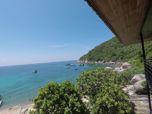 A coastal view with boats on the water, a beach, and a hillside with greenery.