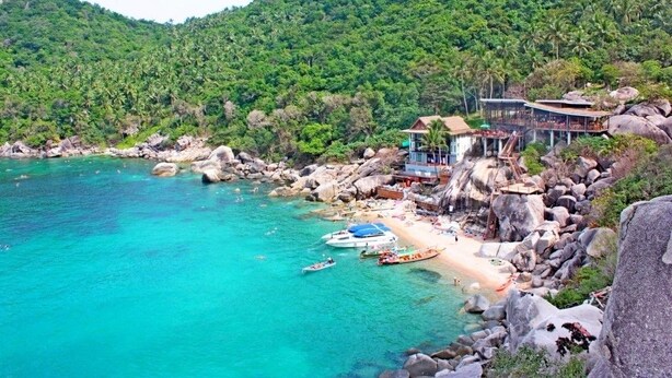A coastal resort with a beach, rocky shoreline, and lush greenery.