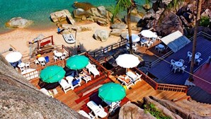 A beachside resort with a wooden deck, lounge chairs, umbrellas, and a view of the turquoise sea.