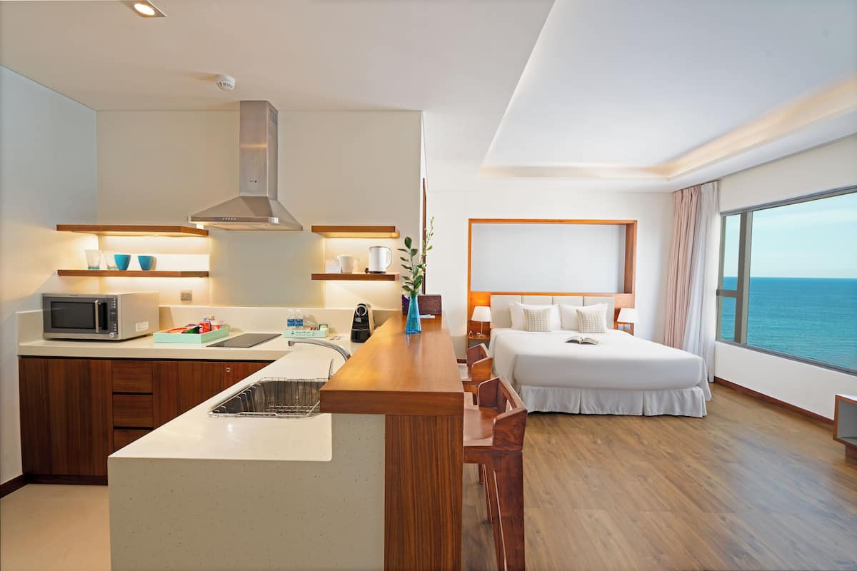 Une chambre d’hôtel moderne dotée d’un coin cuisine, d’un grand lit et offrant une vue sur la mer.