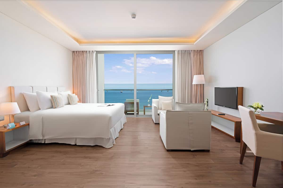 Une chambre d’hôtel avec un lit, un bureau, une chaise, une télévision et une vue sur la mer.
