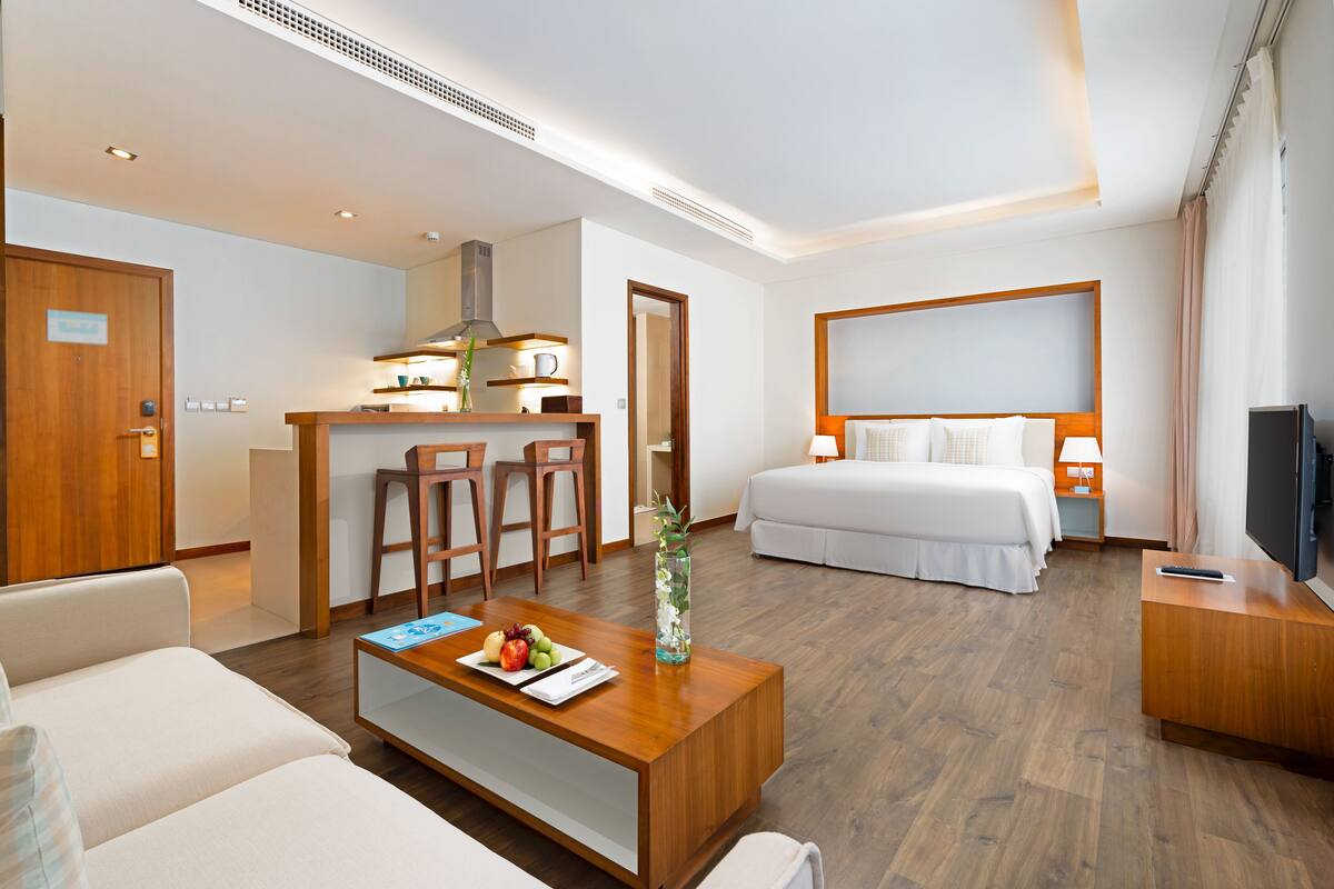 Une chambre d’hôtel moderne équipée d’un lit, d’un canapé, d’une table basse, d’une télévision et d’un coin cuisine.