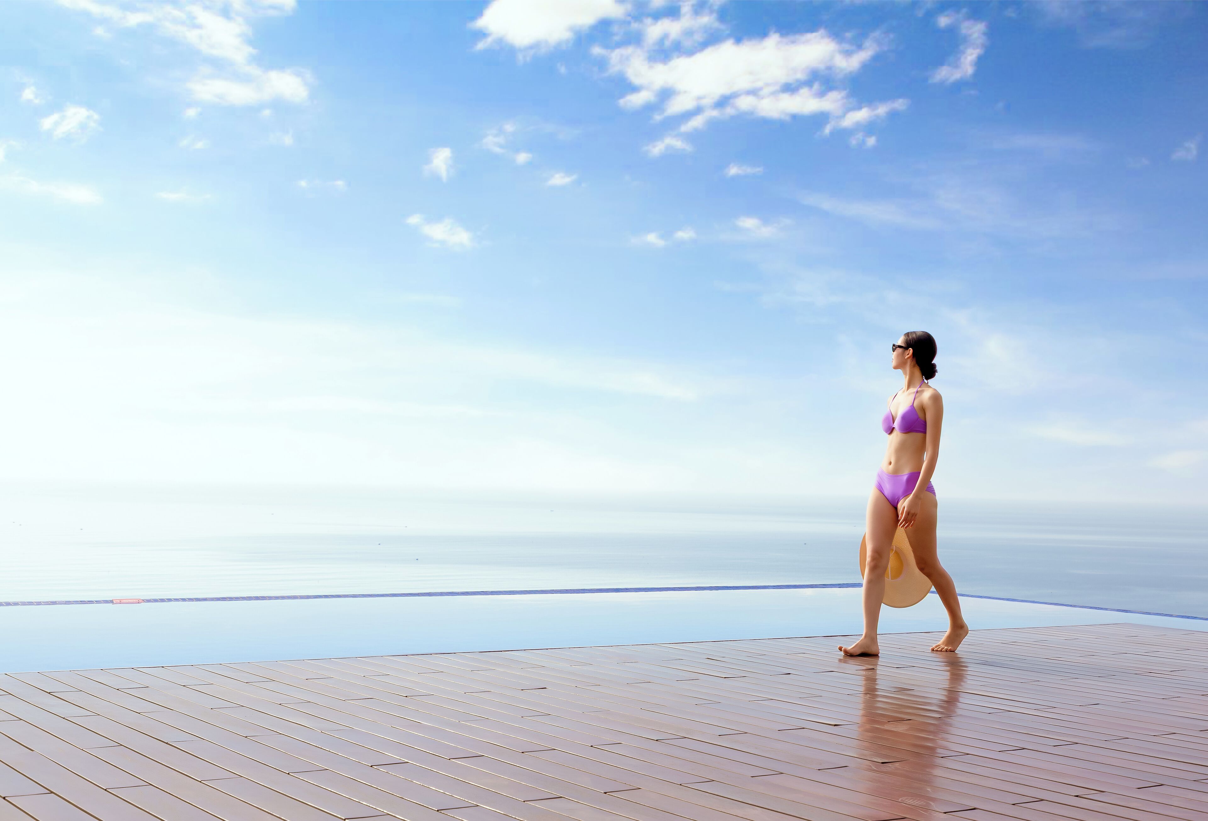 Een vrouw in een paars bikini loopt over een houten dek met uitzicht op de oceaan.