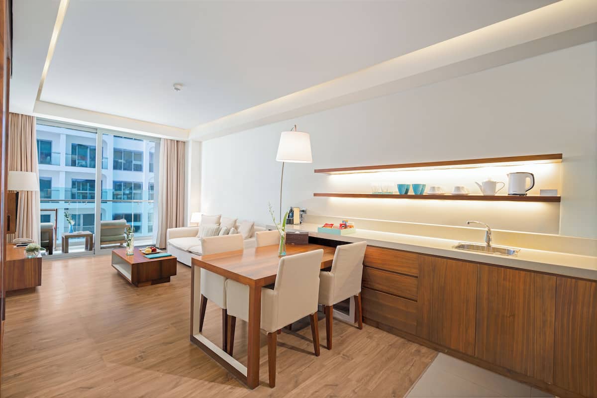 Une chambre d’hôtel moderne avec une table à manger en bois, un canapé et un coin cuisine équipé d’un évier et d’une étagère intégrés.