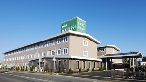 A hotel with a green sign, multiple windows, and a covered parking area. - Hotel Route-Inn Tome (Tome)