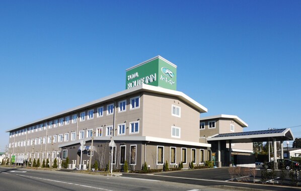 A hotel with a green sign, multiple windows, and a covered parking area.