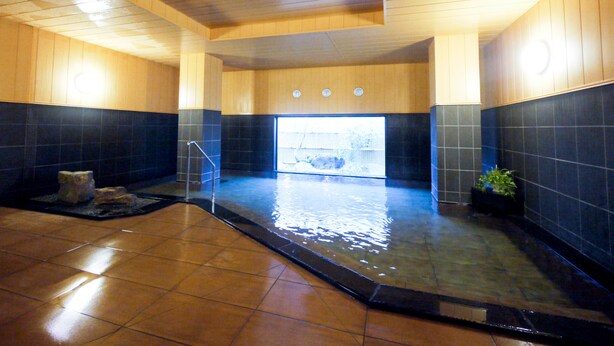A traditional Japanese onsen with wooden walls and a stone floor, a small seating area, and a view of the outside. - Hotel Route-Inn Tome (Tome)