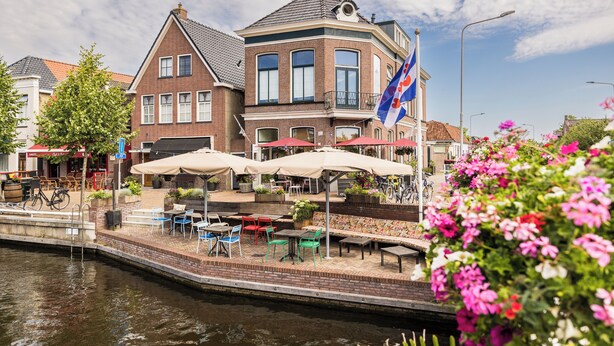 Un café situé au bord de la rivière, avec une terrasse et un drapeau.