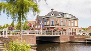 Un bâtiment situé au bord d’un canal, avec un pont, un drapeau et une rangée de fleurs.
