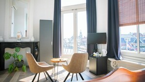 Un salon moderne avec une grande fenêtre, une cheminée, deux fauteuils, une petite table et un téléviseur.