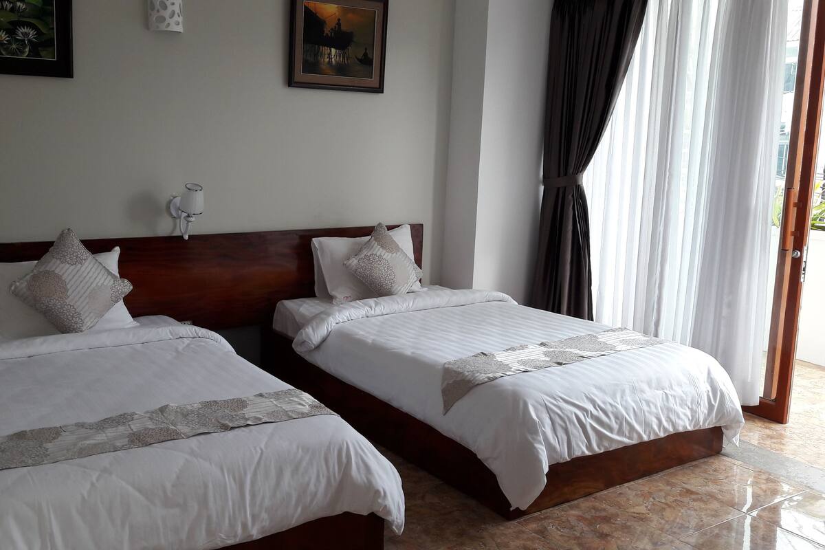 Een hotelkamer met twee bedden, een houten hoofdbord, witte beddengoed en een groot raam met gordijnen.