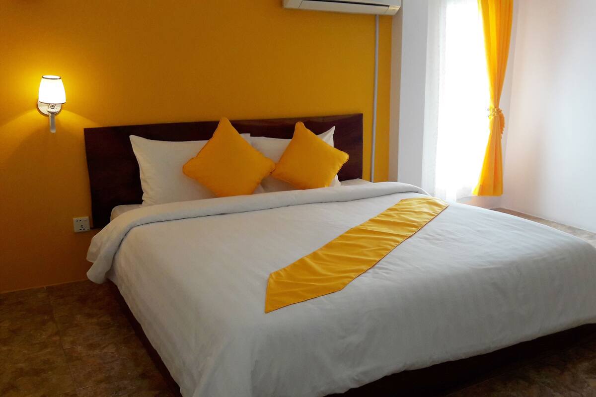 Hotelkamer met een bed, hoofdbord, een wandlamp en een raam met gordijnen.
