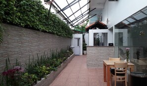 A modern indoor garden with a glass ceiling, a stone wall, and a small seating area with a table and chairs. - The Flora Boutique Hotel (Phnom Penh)
