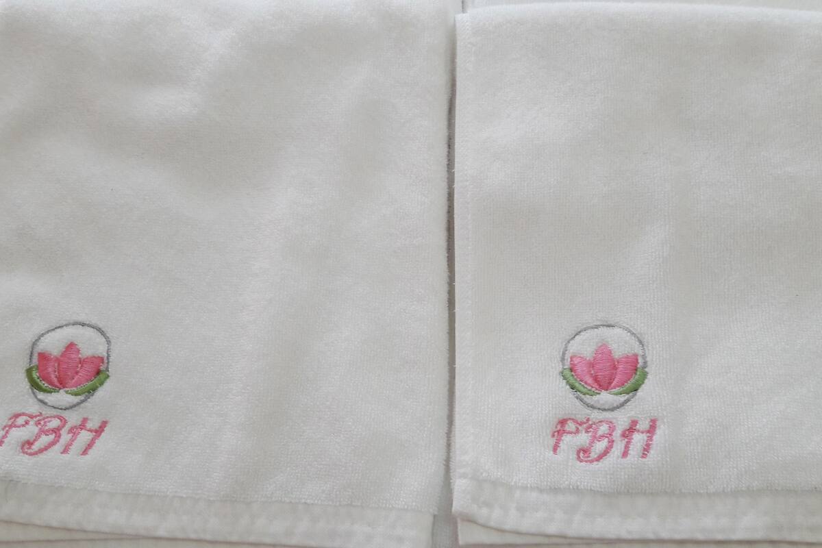 Een witte handdoek met geborduurde roze bloemen en de letters 'PBH'.
