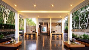 A modern reception area with two reception desks, a central walkway, and a view of the outdoors. - Wanaburi Hotel (Thep Kasattri)