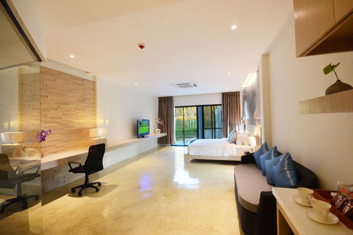 A modern hotel room with a large bed, a desk with a chair, a TV, and a view of the outdoors.