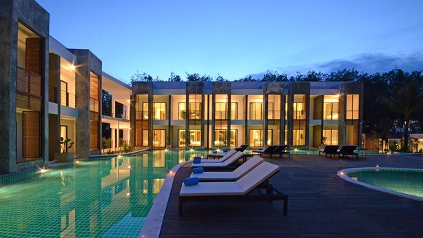 A modern resort with a swimming pool, lounge chairs, and a well-lit building facade. - Wanaburi Hotel (Thep Kasattri)
