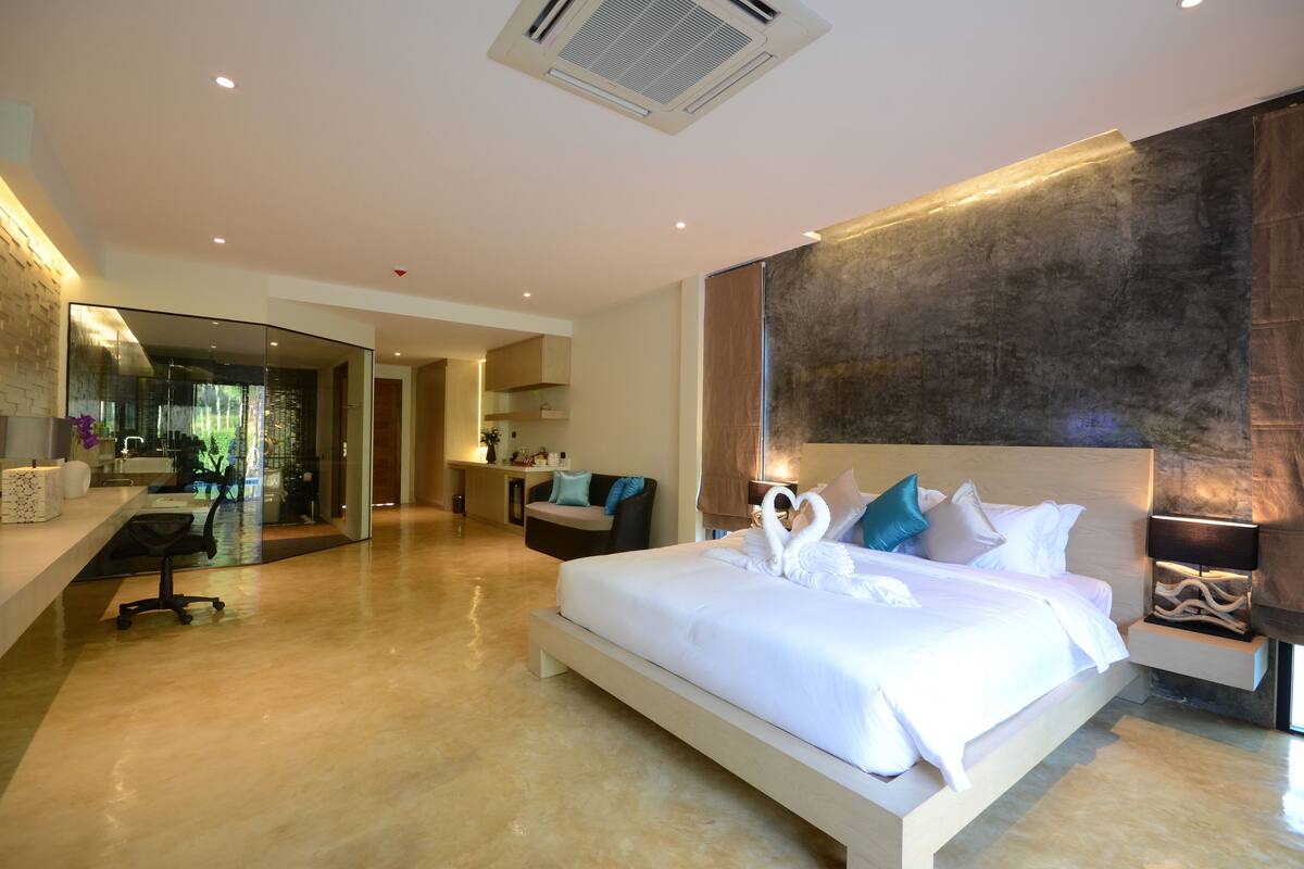A modern hotel room with a large bed, a desk, and a bathroom visible through a glass partition.