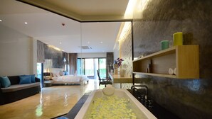 A modern hotel room with a large bathtub filled with rose petals, a sofa, a dining area, and a view of the outdoors. - Wanaburi Hotel (Thep Kasattri)