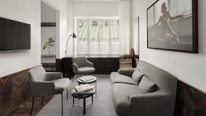 A modern living room with a grey sofa, two armchairs, a coffee table, and a TV. There is a large window with curtains and a framed picture on the wall. - Miss Clara by Nobis, Stockholm, a Member of Design Hotels (Stockholm)