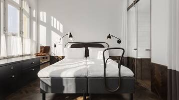 A modern bedroom with a bed, bedside lamps, a dresser, and a view of the outdoors through large windows.