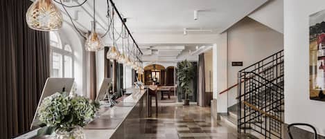 A modern hotel lobby with a check-in counter, a staircase, and a large potted plant.