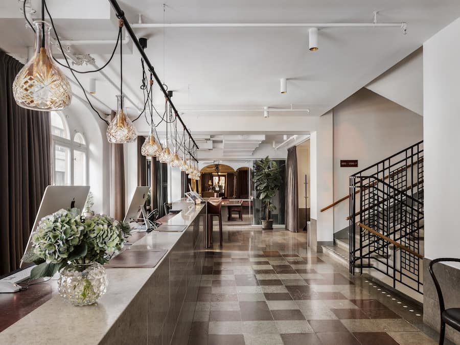 Un moderno vestíbulo de hotel con un mostrador de recepción, una escalera y una planta grande en maceta.