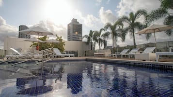 Una piscina al aire libre, sombrillas, sillones reclinables de piscina