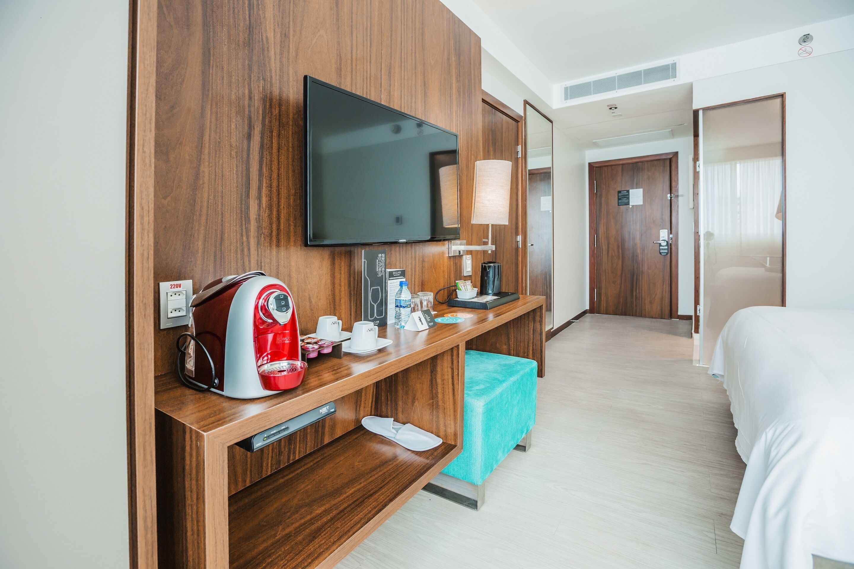 Une chambre d’hôtel avec un bureau en bois, un téléviseur à écran plat, une machine à café et un lit.