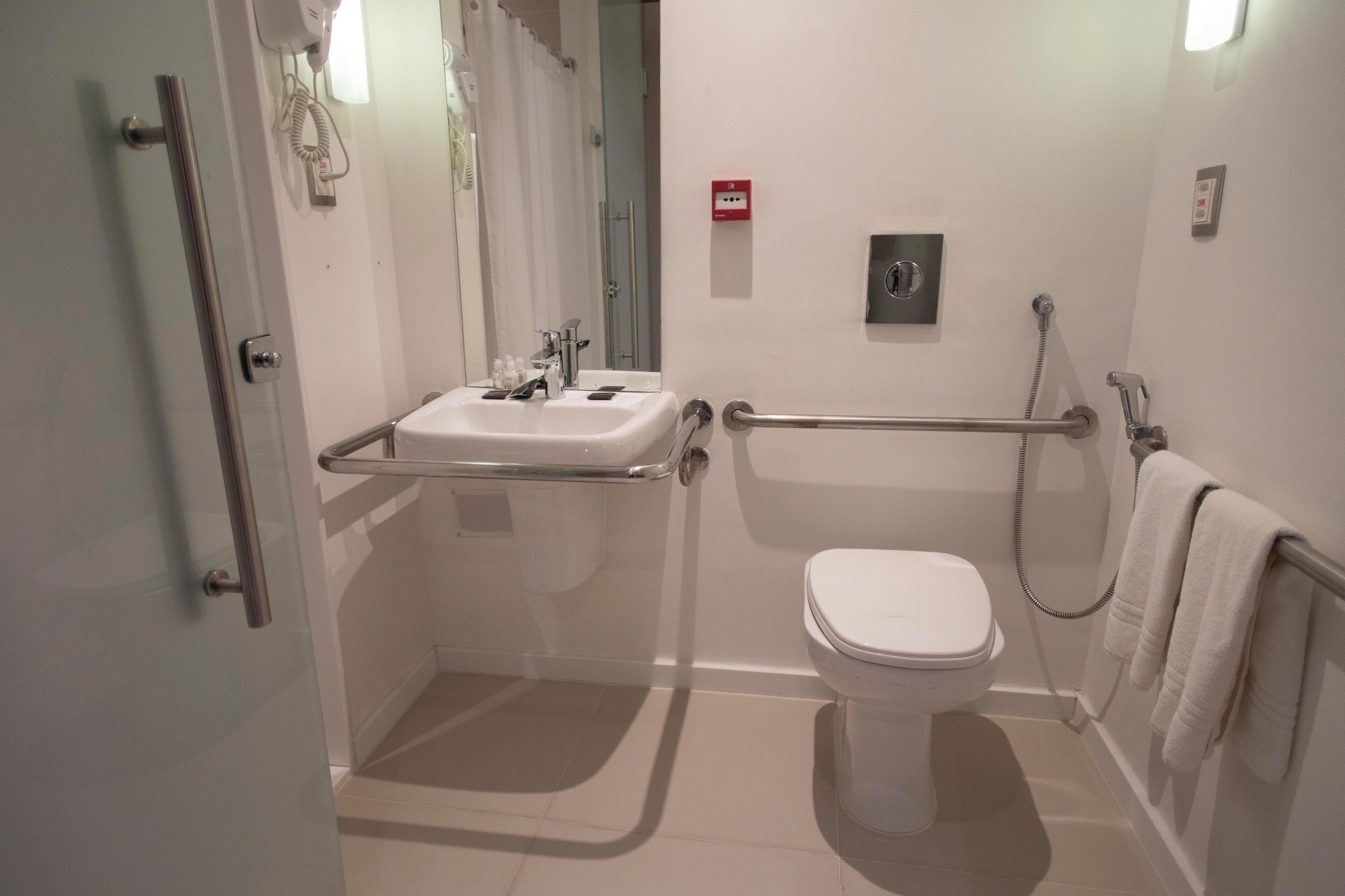 Un bagno moderno con box doccia in vetro, lavandino bianco, water e mancorrente.