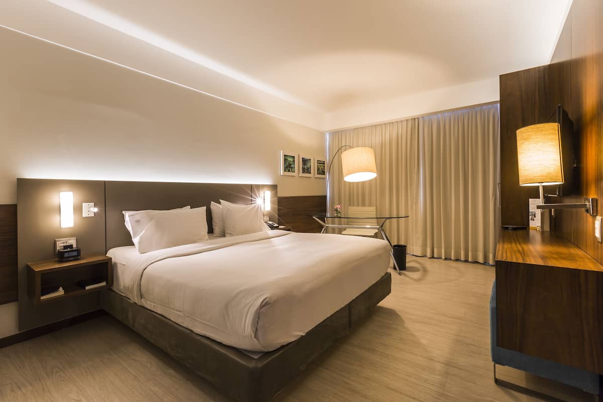 A modern hotel room with a large bed, bedside tables, a desk, and a lamp.